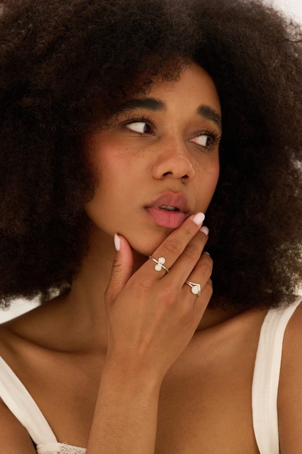Model wearing the Amara Breastmilk Ring on index finger, stacked with a teardrop breastmilk ring and wishbone stacking ring in a close-up hand shot.